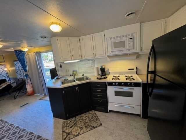 kitchen with black refrigerator, white microwave, sink, white cabinets, and range