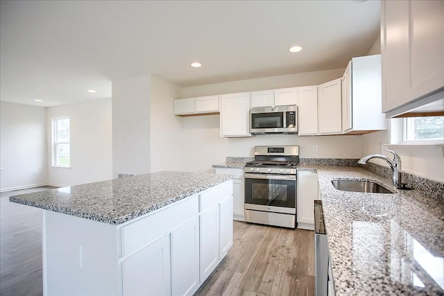 kitchen featuring light stone counters, stainless steel appliances, a sink, a kitchen island, and white cabinetry