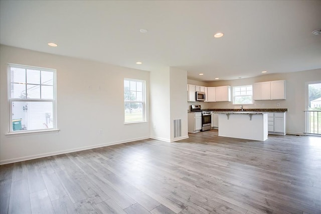 unfurnished living room featuring baseboards, light wood finished floors, a sink, and recessed lighting