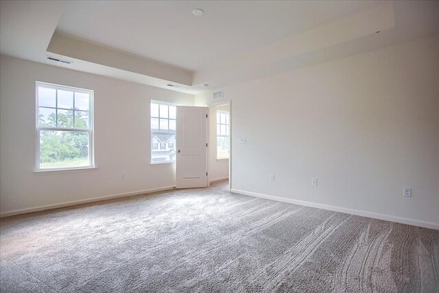 carpeted empty room with a tray ceiling, visible vents, and baseboards