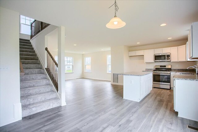 kitchen with stainless steel appliances, a sink, white cabinets, a center island, and decorative light fixtures