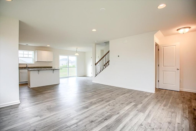 unfurnished living room with light wood-style flooring, stairs, baseboards, and recessed lighting