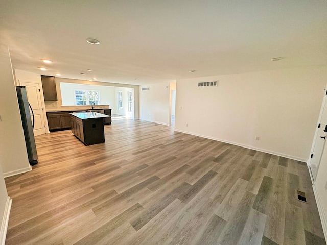 unfurnished living room featuring visible vents, a sink, light wood-style flooring, and baseboards