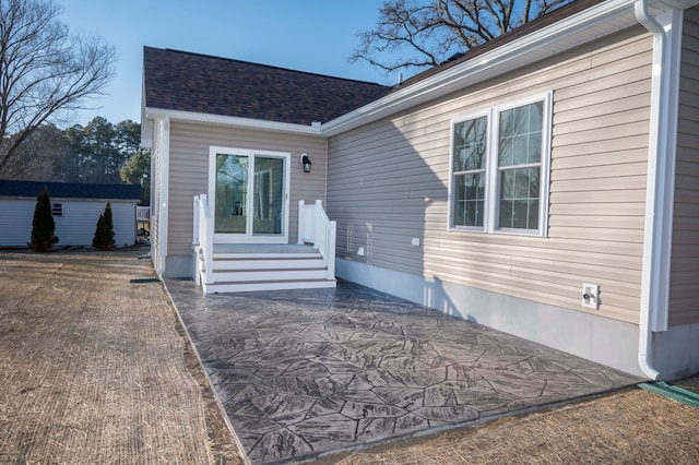 property entrance with roof with shingles and a patio