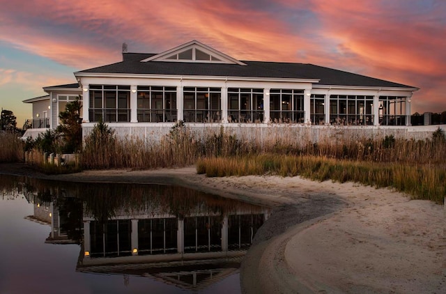 back of property at dusk featuring a water view and a sunroom