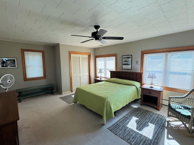 bedroom featuring a baseboard heating unit, light colored carpet, ceiling fan, and a closet