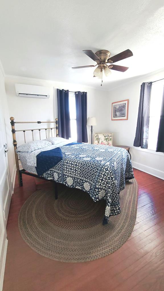 bedroom with dark hardwood / wood-style floors, a wall mounted AC, and ceiling fan