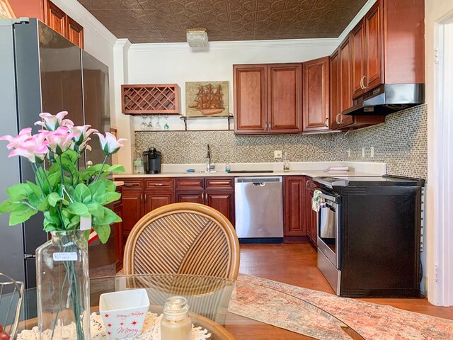 kitchen with appliances with stainless steel finishes, tasteful backsplash, crown molding, sink, and wood-type flooring