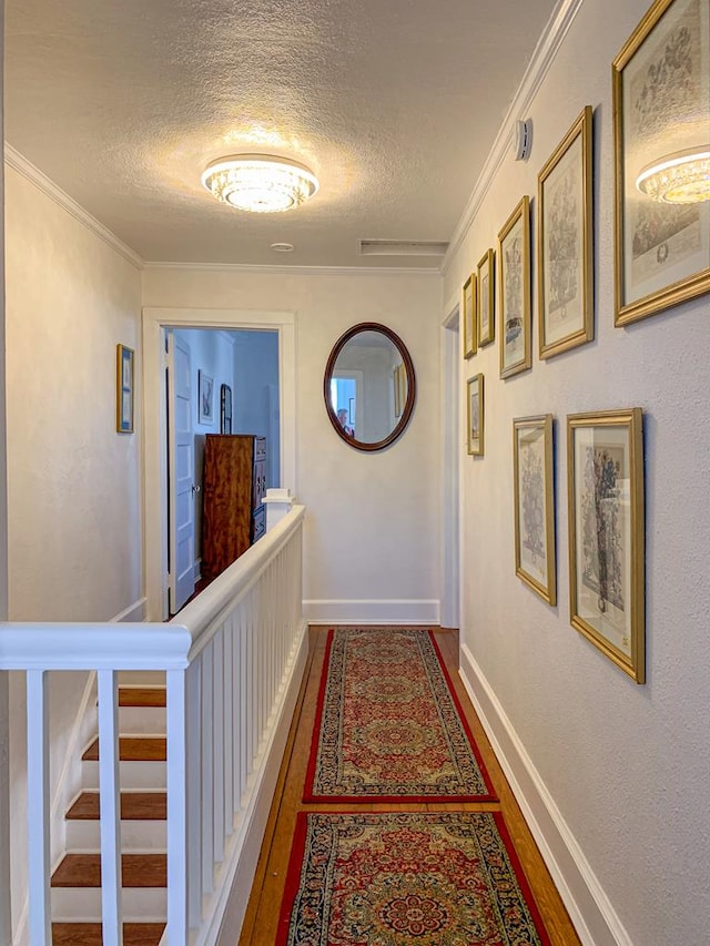 corridor with hardwood / wood-style floors, ornamental molding, and a textured ceiling