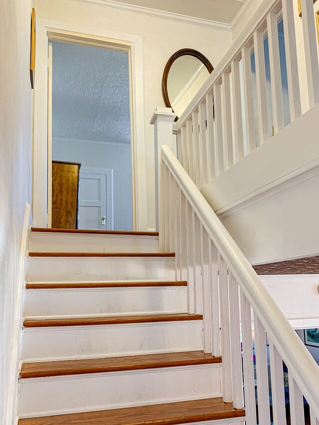 stairway featuring ornamental molding and a textured ceiling