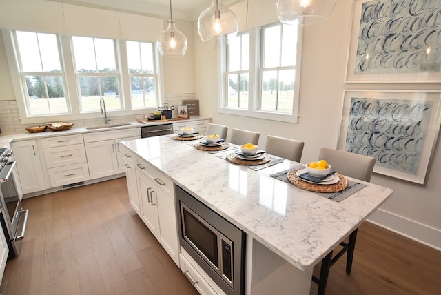 kitchen featuring sink, light stone countertops, appliances with stainless steel finishes, a kitchen island, and white cabinetry