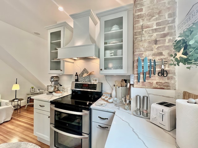 2453 Sand Hill Dr, Cape Charles, VA 23310 - kitchen featuring range with two ovens, custom exhaust hood, light stone counters, light wood-style flooring, and glass insert cabinets