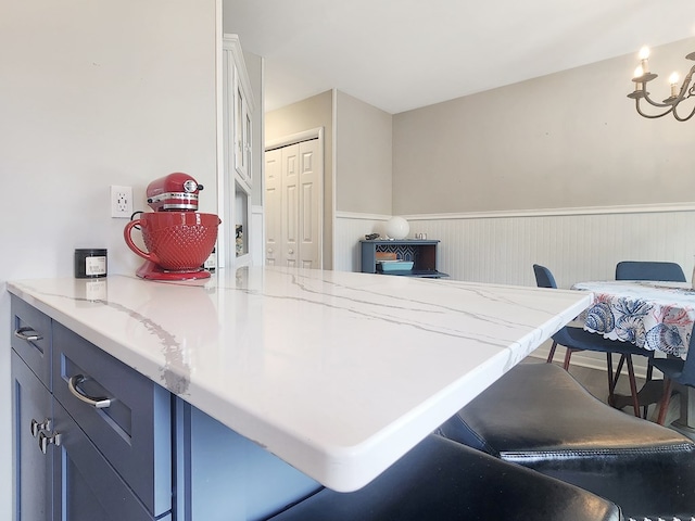 7207 Bunting Rd, Chincoteague, VA 23336 - kitchen with a wainscoted wall, a chandelier, light stone countertops, white cabinets, and a breakfast bar area