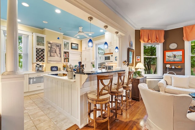 306 Bay Ave, Cape Charles, VA 23310 - kitchen featuring crown molding, a ceiling fan, a warming drawer, a breakfast bar, and radiator heating unit