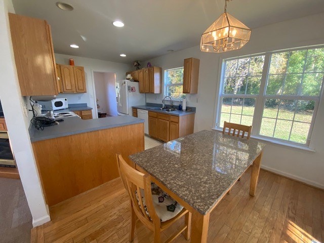 kitchen with decorative light fixtures, light wood-type flooring, white appliances, and sink