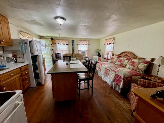 interior space with dark hardwood / wood-style floors, a breakfast bar, white electric stove, a center island, and a textured ceiling