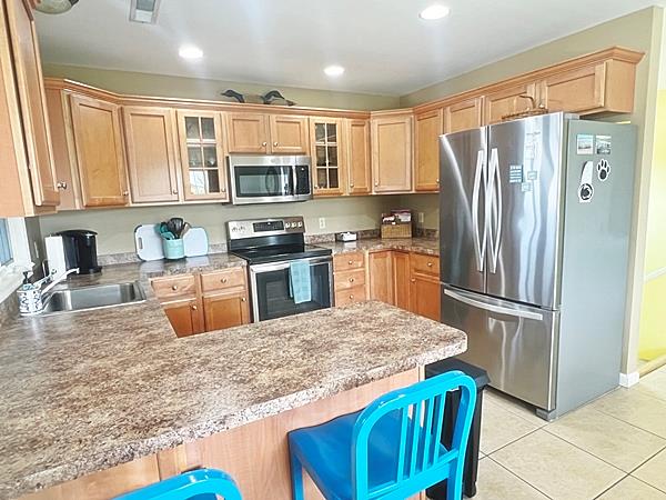 5061 Bay Colony Ln, Chincoteague, VA 23336 - kitchen with stainless steel appliances, a peninsula, a sink, glass insert cabinets, and light tile patterned floors