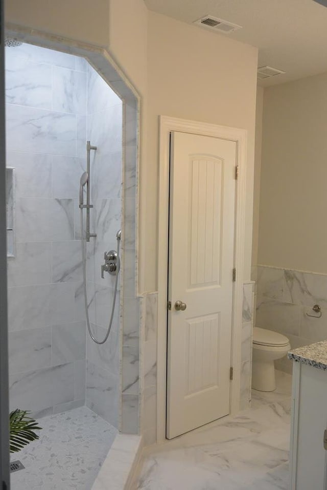 bathroom with tiled shower, vanity, toilet, and tile walls