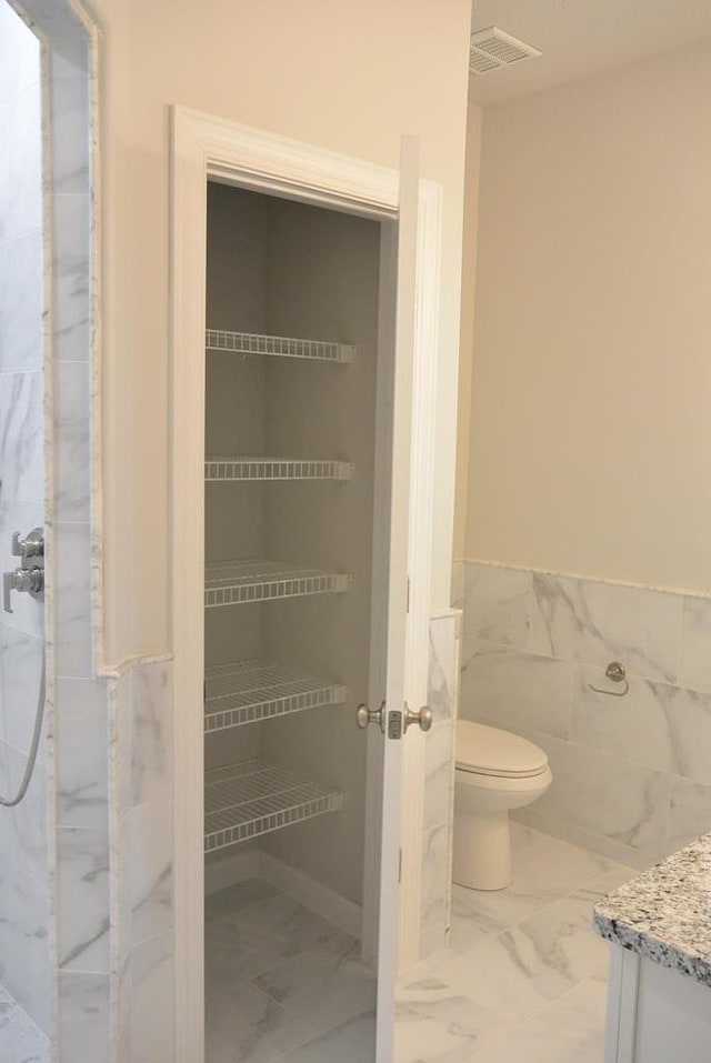 bathroom featuring vanity, tile walls, and toilet