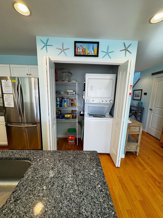 laundry room featuring stacked washer / drying machine and light hardwood / wood-style flooring