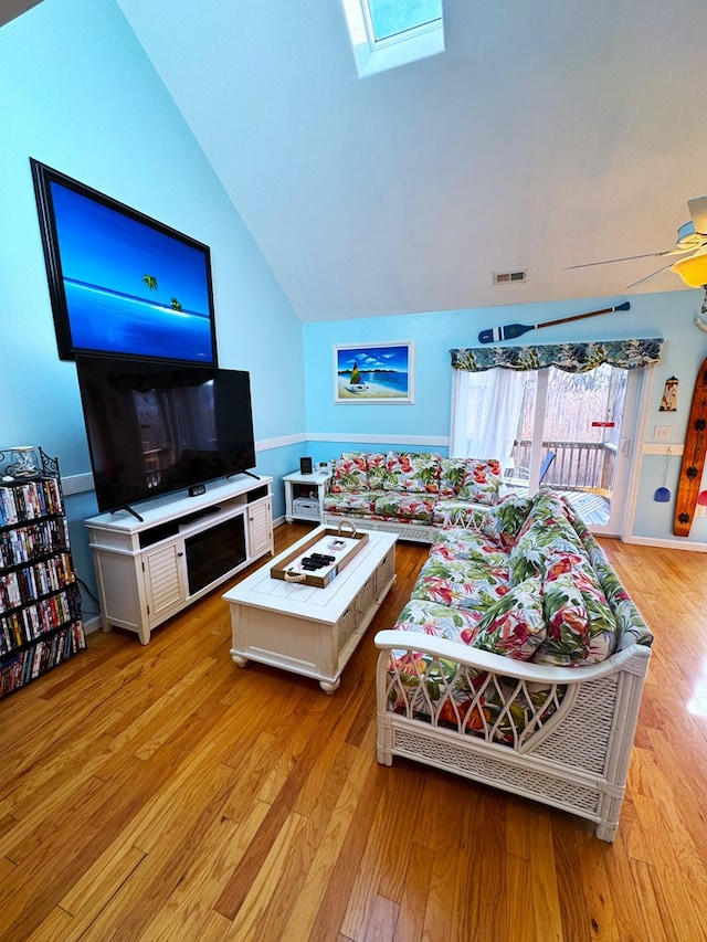 living room featuring ceiling fan, vaulted ceiling with skylight, and light hardwood / wood-style flooring