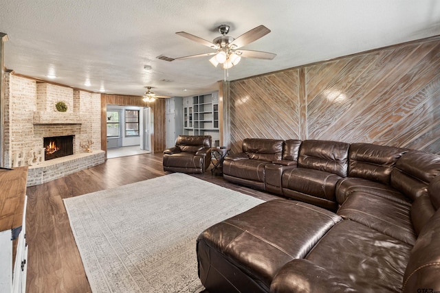 living room featuring ceiling fan, dark wood-type flooring, wood walls, a textured ceiling, and a fireplace