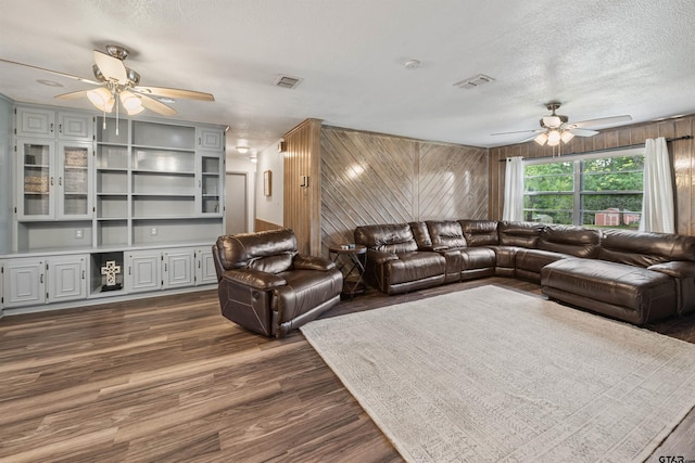 living room with ceiling fan, dark hardwood / wood-style flooring, a textured ceiling, and wooden walls