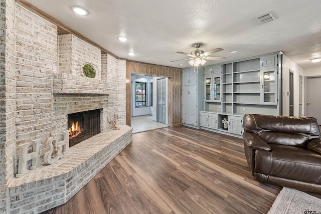 living room with ceiling fan, a brick fireplace, dark hardwood / wood-style flooring, crown molding, and a textured ceiling