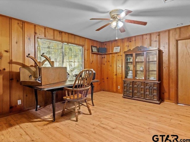 home office with light hardwood / wood-style flooring, wooden walls, and ceiling fan