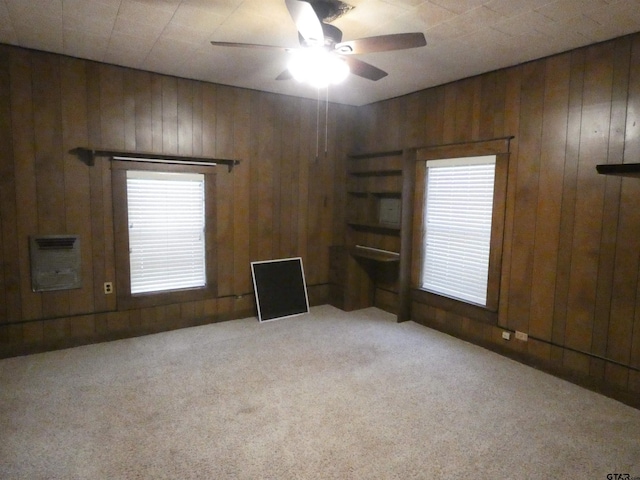 carpeted empty room with heating unit, ceiling fan, and wooden walls