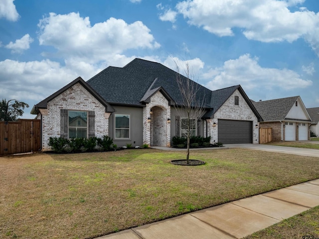 french provincial home featuring a front lawn, fence, concrete driveway, an attached garage, and a shingled roof