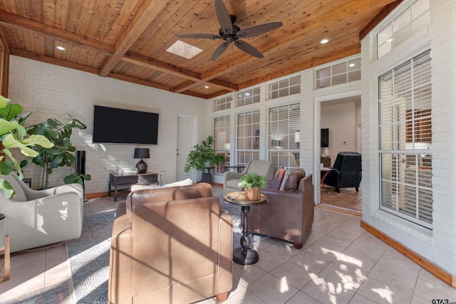 tiled living room with wooden ceiling, a skylight, brick wall, ceiling fan, and beam ceiling