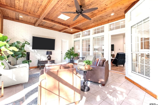 tiled living room featuring a skylight, wooden ceiling, ceiling fan, brick wall, and beam ceiling