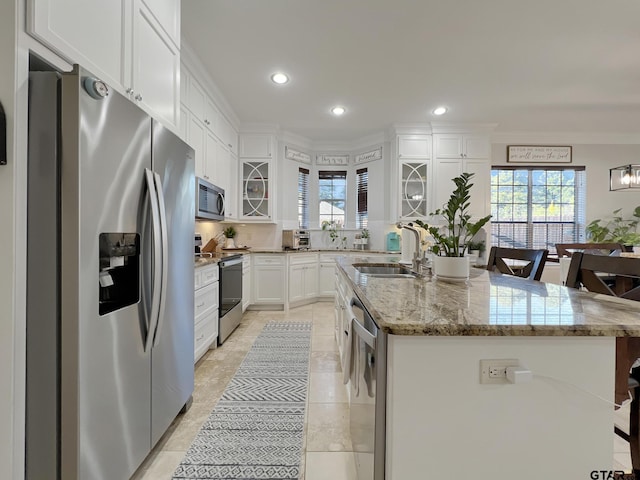 kitchen featuring appliances with stainless steel finishes, an island with sink, sink, white cabinets, and a kitchen bar