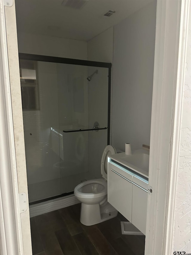 bathroom featuring hardwood / wood-style floors, vanity, a shower with shower door, and toilet