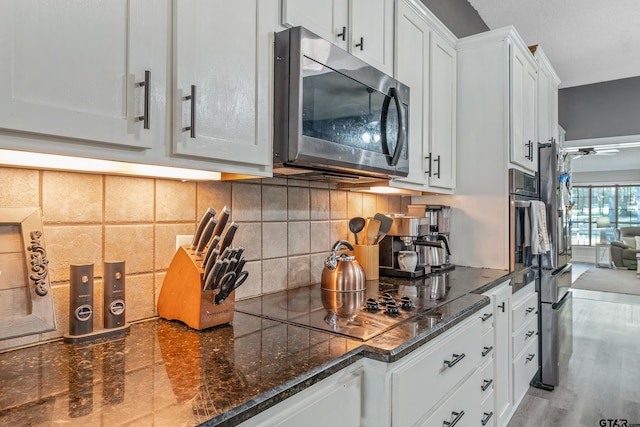 kitchen featuring white cabinetry, dark stone counters, black electric stovetop, backsplash, and light wood-type flooring