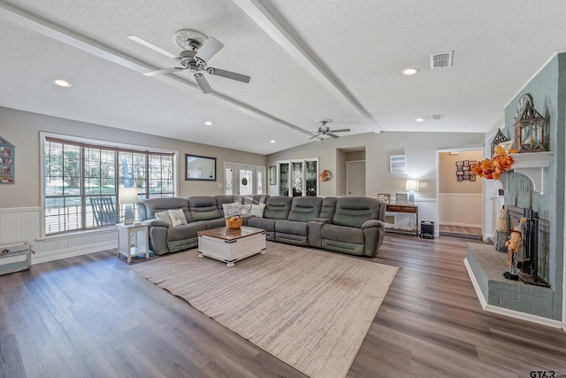 living room with ceiling fan, a textured ceiling, vaulted ceiling with beams, a brick fireplace, and dark hardwood / wood-style flooring