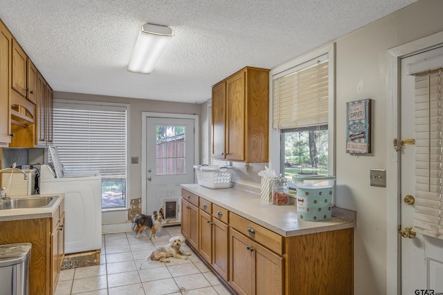 kitchen with washer / dryer, a textured ceiling, light tile patterned floors, and sink