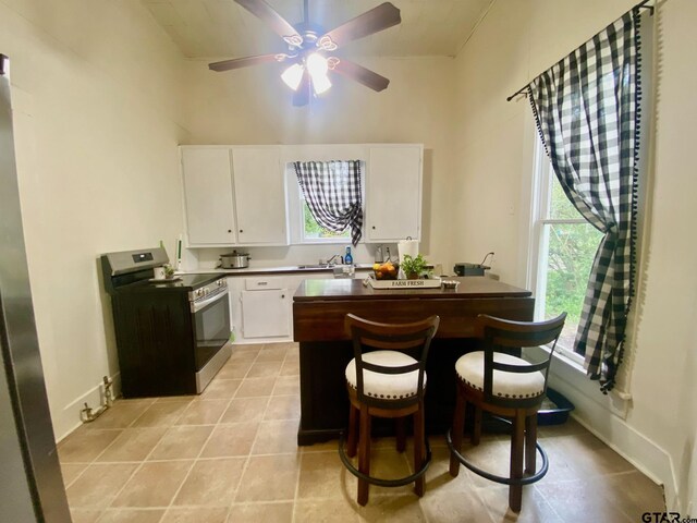138 S Grace St, Crockett, TX 75835 - kitchen with stainless steel range with electric stovetop, white cabinetry, a ceiling fan, a towering ceiling, and a kitchen bar