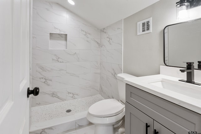 bathroom with tiled shower, vanity, vaulted ceiling, and toilet