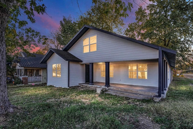 back house at dusk featuring a lawn and a porch