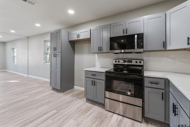 kitchen featuring gray cabinetry, light hardwood / wood-style flooring, light stone countertops, tasteful backsplash, and stainless steel appliances