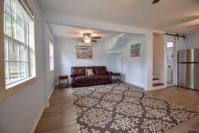 living area with a barn door, baseboards, a ceiling fan, and wood finished floors