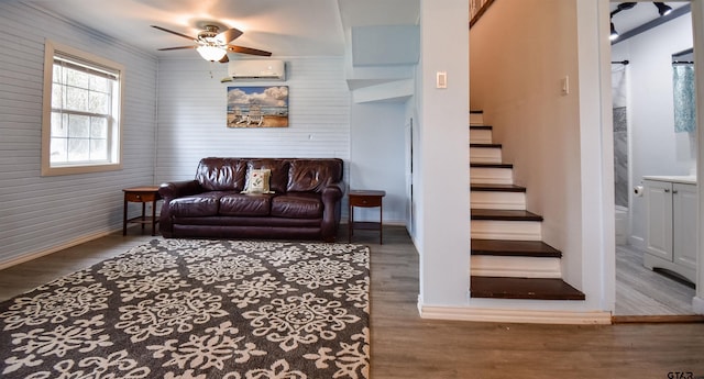 living area with stairway, a wall unit AC, wood finished floors, and a ceiling fan