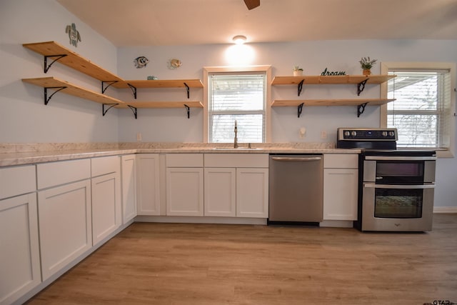 kitchen featuring stainless steel appliances, a sink, light wood finished floors, and open shelves