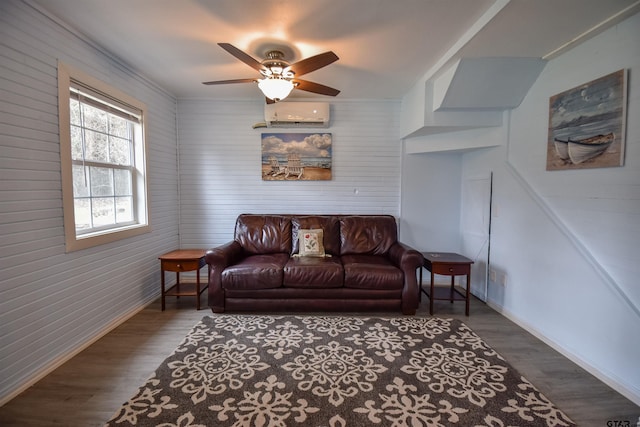 living room featuring a ceiling fan, a wall unit AC, baseboards, and wood finished floors