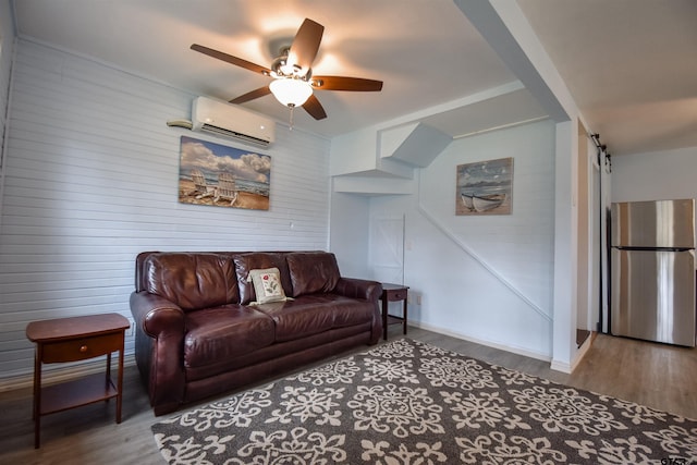 living room with ceiling fan, a barn door, wood finished floors, baseboards, and a wall mounted air conditioner