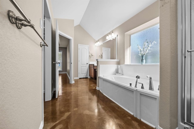 bathroom featuring concrete flooring, vanity, vaulted ceiling, and a tub