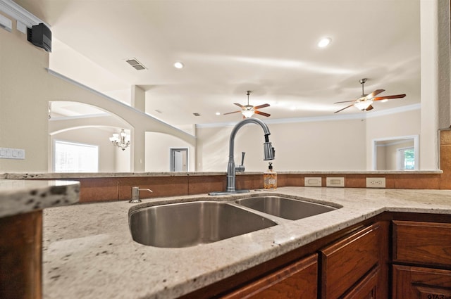 kitchen with a healthy amount of sunlight, light stone counters, crown molding, and sink