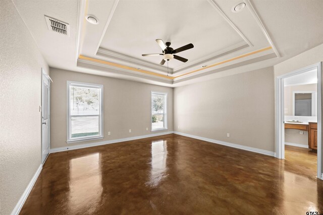 empty room with ceiling fan, a raised ceiling, crown molding, and concrete floors